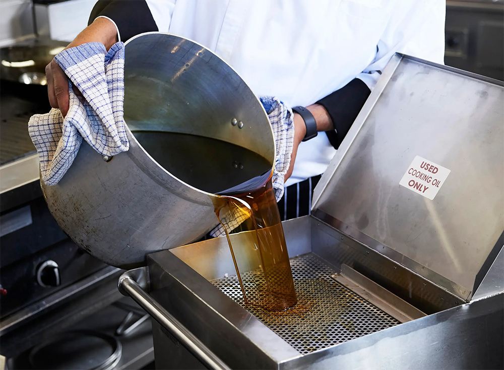 Somebody pouring used cooking oil from a pot into a disposal device.